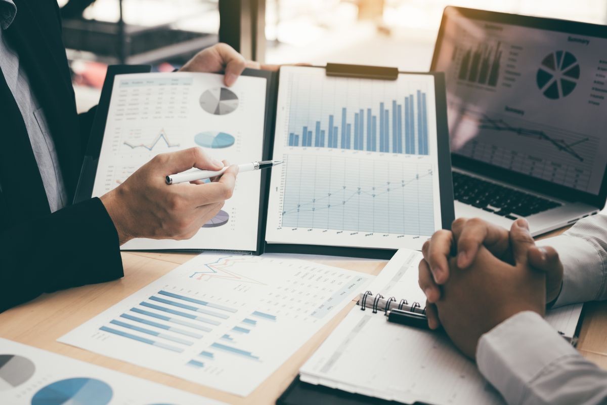 Two people discussing financial charts and graphs on paper and a laptop during a meeting.