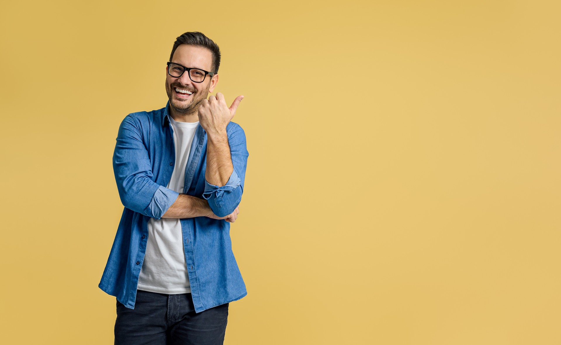 Glücklicher gutaussehender Unternehmer, der mit dem Daumen auf die Textfläche für Werbung vor gelbem Hintergrund zielt